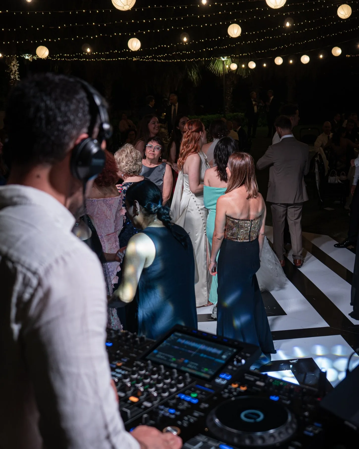Wedding DJ watching guests on the dance floor under string lights